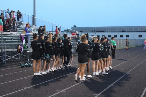 The cheerleaders stand for the national anthem.