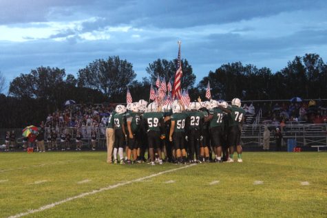 The football team huddles around the flag before the game begins.