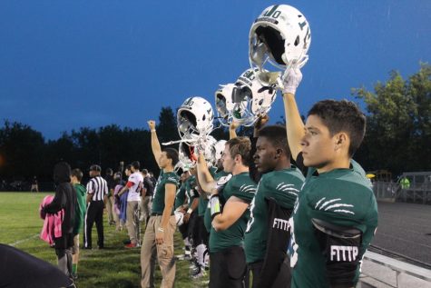 The team lifts their helmets for kickoff.